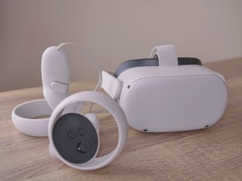 Photo of Modern virtual reality headset and controllers on wooden table