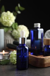 Photo of Spa composition. Cosmetic products, burning candle and hydrangea flowers on gray table against black background