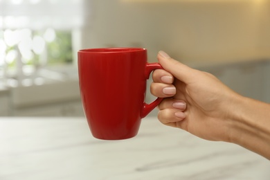 Woman holding elegant red cup in kitchen, closeup 