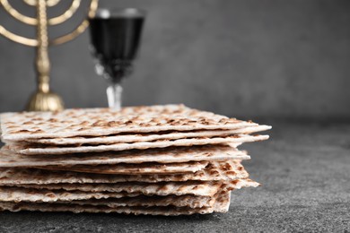 Photo of Stack of traditional matzos near red wine on grey table, closeup