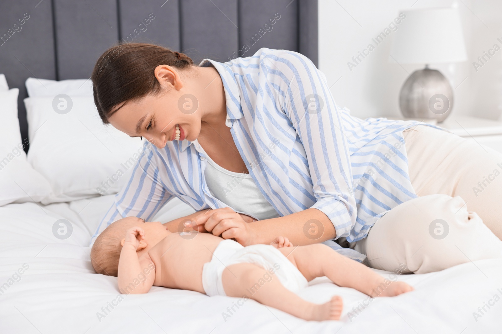 Photo of Happy young woman applying body cream onto baby`s skin on bed