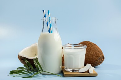 Photo of Delicious vegan milk, coconuts and leaf on light blue background
