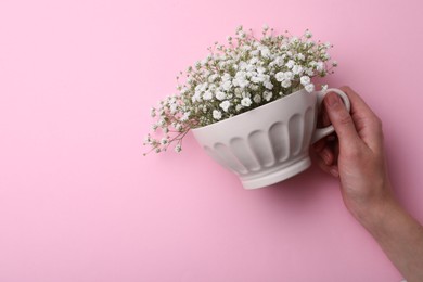 Photo of Top view of woman holding white cup with gypsophila on pink background, closeup Space for text