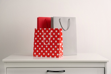 Photo of Paper shopping bags on white chest of drawers against light background