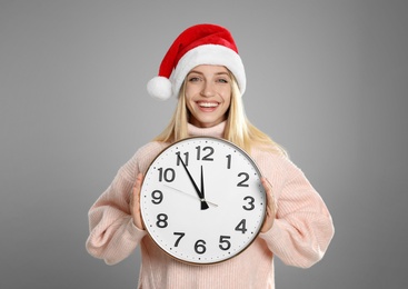 Woman in Santa hat with clock on grey background. New Year countdown