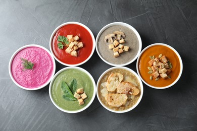 Different tasty cream soups in bowls on dark grey table, flat lay