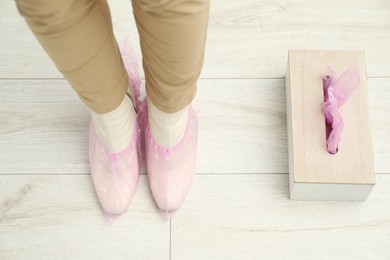 Photo of Woman wearing pink shoe covers onto her boots indoors, top view