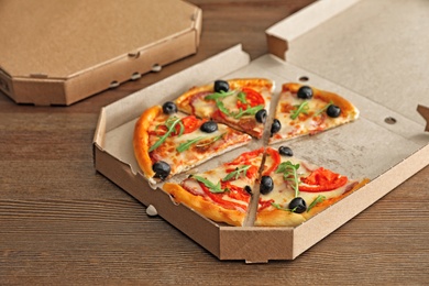Photo of Cardboard box with tasty pizza on wooden background