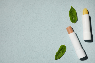 Photo of Hygienic lipsticks and mint leaves on light green background, flat lay. Space for text