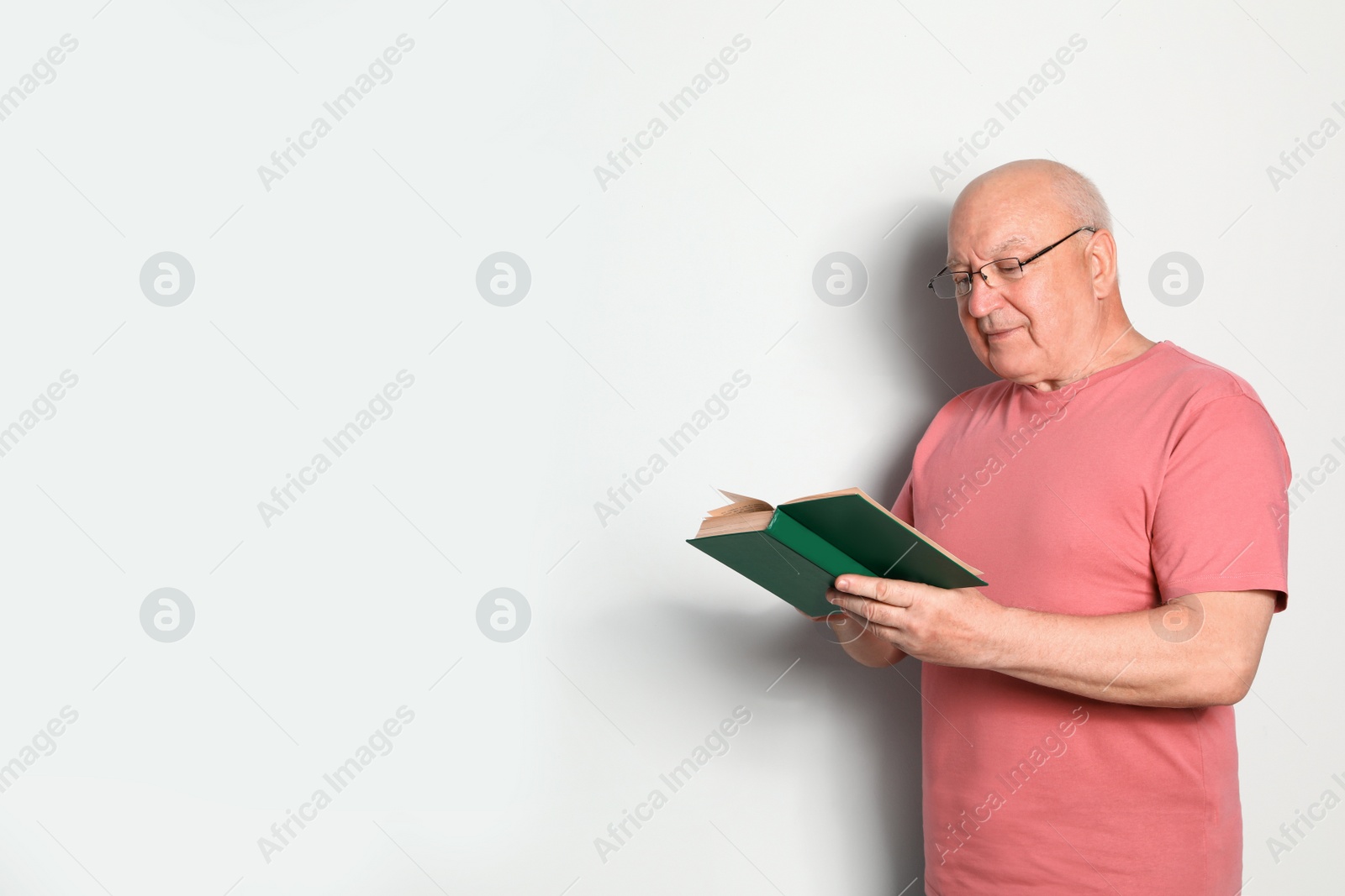 Photo of Portrait of senior man with glasses reading book on light background. Space for text