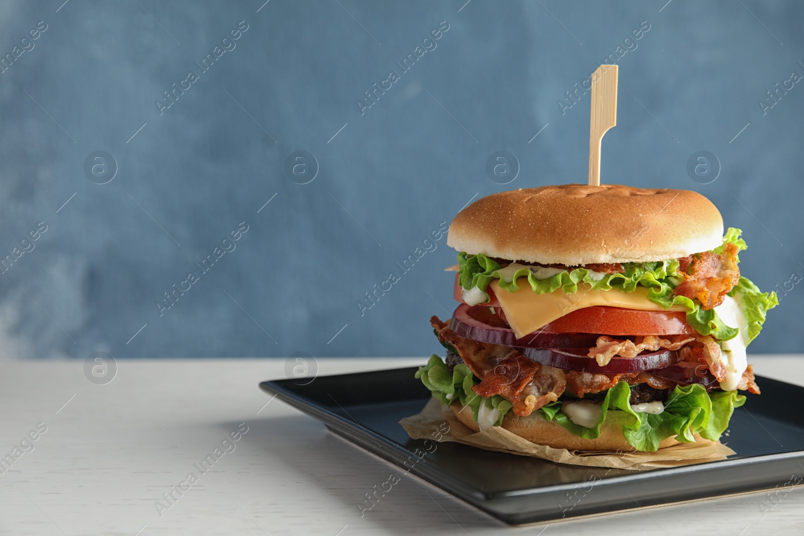 Photo of Plate of tasty burger with bacon on table. Space for text