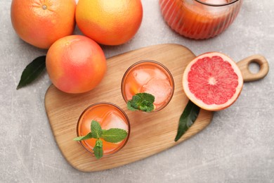 Photo of Tasty freshly made grapefruit juice, fruits and mint on light grey table, flat lay