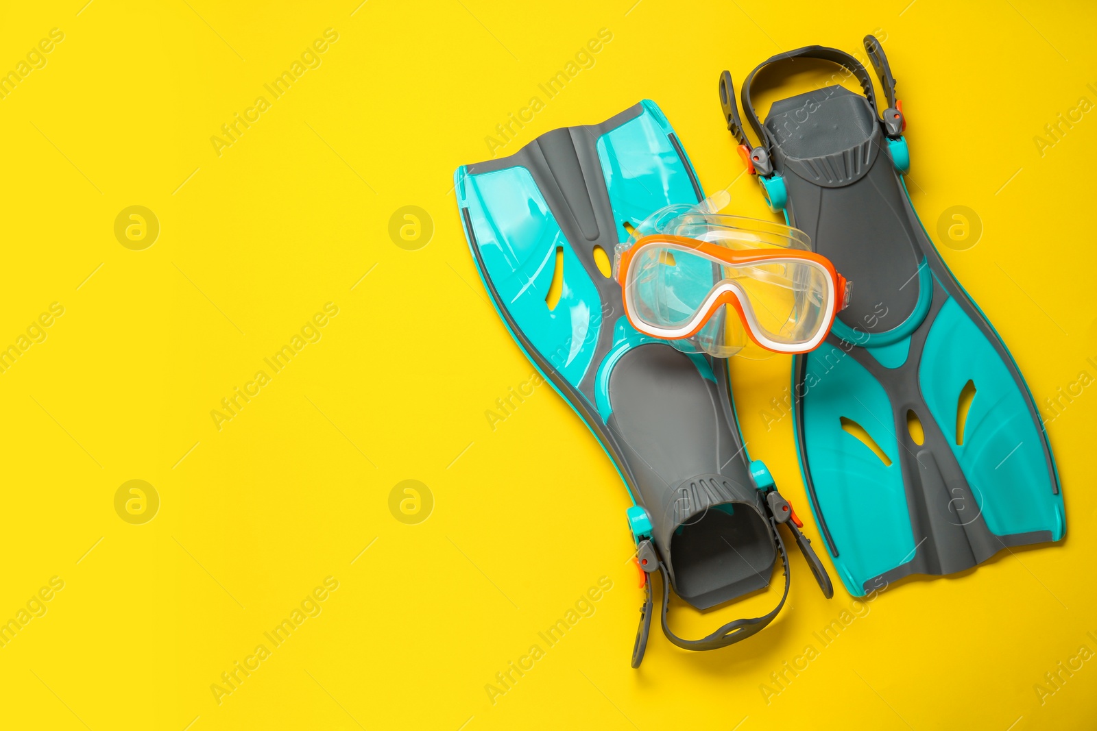 Photo of Pair of turquoise flippers and mask on yellow background, flat lay. Space for text