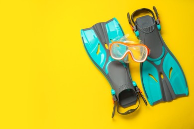 Pair of turquoise flippers and mask on yellow background, flat lay. Space for text