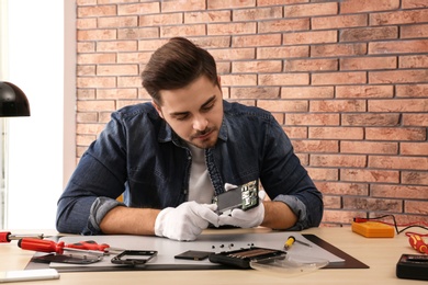 Photo of Technician repairing broken smartphone at table in workshop