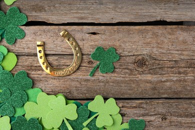 Photo of St. Patrick's day. Golden horseshoe and green decorative clover leaves on wooden table, flat lay