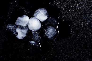 Photo of Melting ice cubes and water drops on black background, top view. Space for text