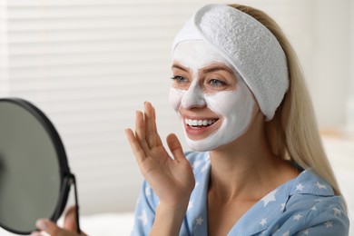 Photo of Young woman with face mask looking into mirror at home. Spa treatments