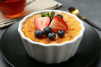 Photo of Delicious creme brulee with berries and mint in bowl on table, closeup