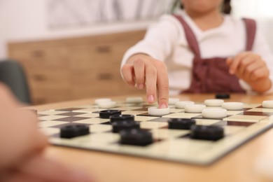 Girl playing checkers at table in room, closeup