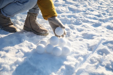 Woman rolling snowballs outdoors on winter day, closeup