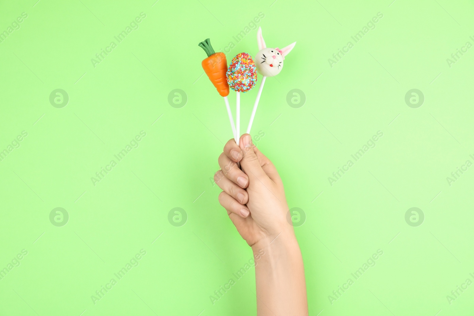 Photo of Woman with delicious cake pops on light green background, closeup. Easter holiday