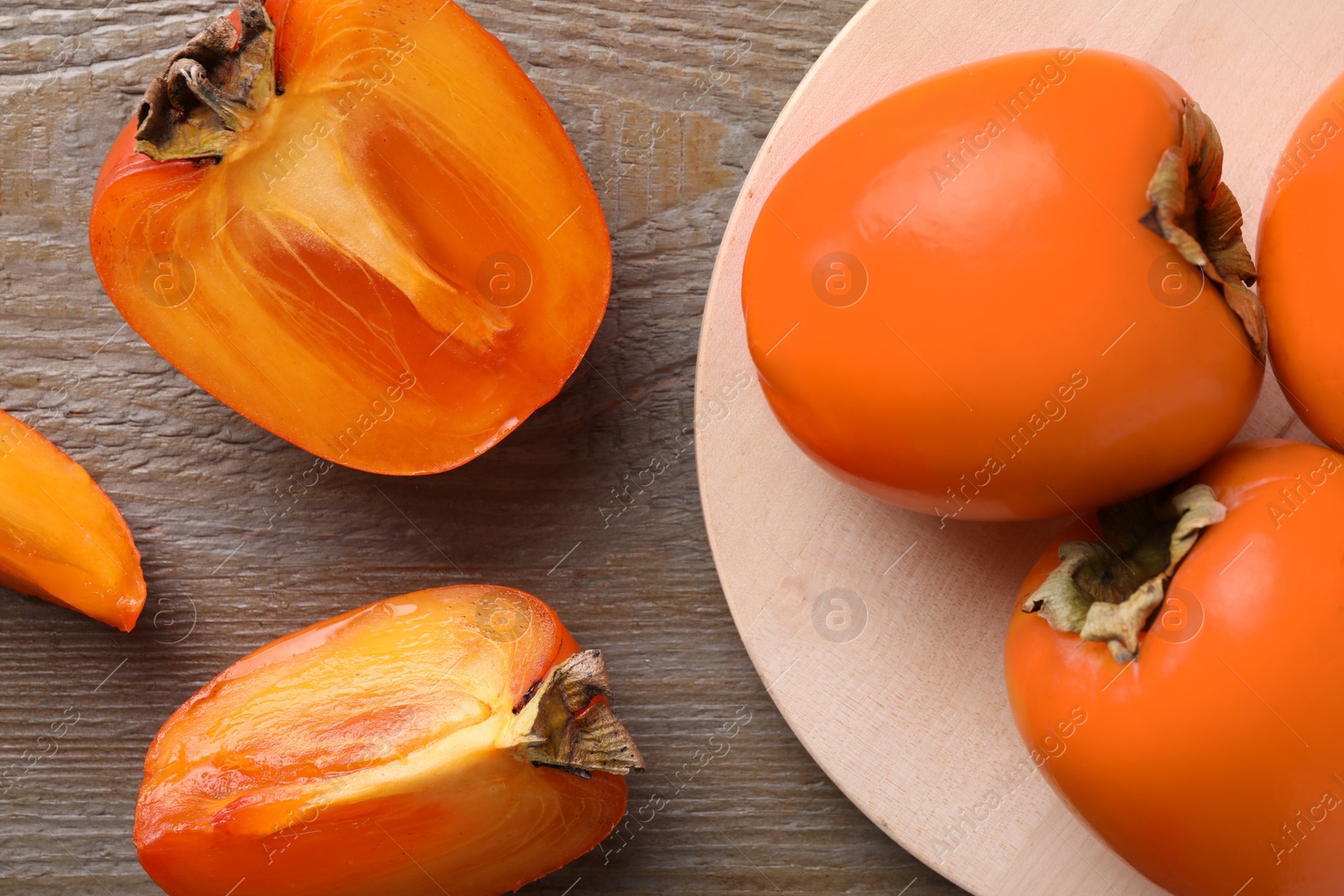 Photo of Whole and cut delicious ripe persimmons on wooden table, flat lay