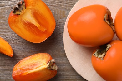 Photo of Whole and cut delicious ripe persimmons on wooden table, flat lay