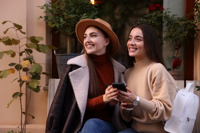 Photo of Happy friends with smartphone resting near building outdoors