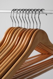 Photo of Wooden clothes hangers on metal rail against light grey background, closeup