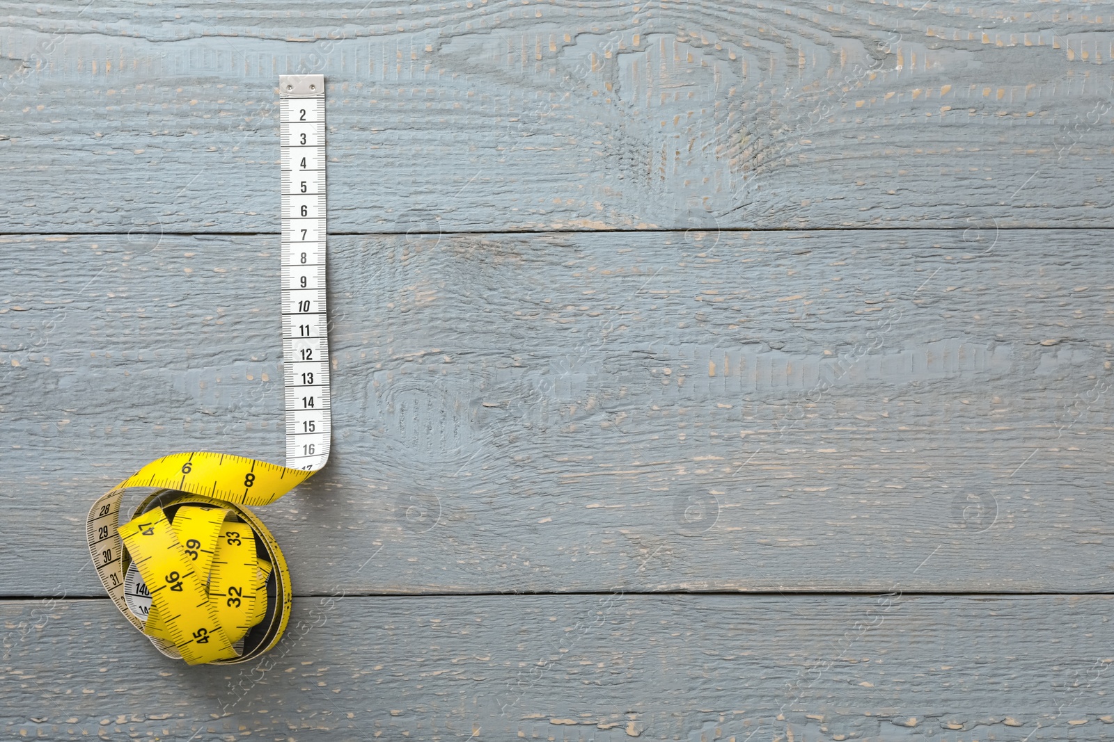 Photo of Yellow measuring tape on light grey wooden table, top view. Space for text