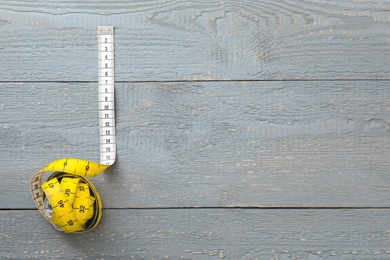 Photo of Yellow measuring tape on light grey wooden table, top view. Space for text