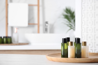 Photo of Wooden tray with mini bottles of cosmetic products on white table in bathroom. Space for text