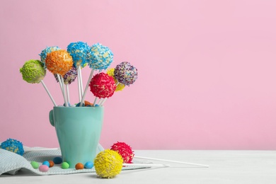 Photo of Cup with tasty cake pops on white table against pink background, space for text