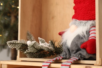 Photo of Christmas gnome and decorative fir twig with snow in wooden box, closeup view