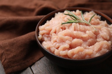 Photo of Fresh raw minced meat and rosemary in bowl on wooden table, closeup