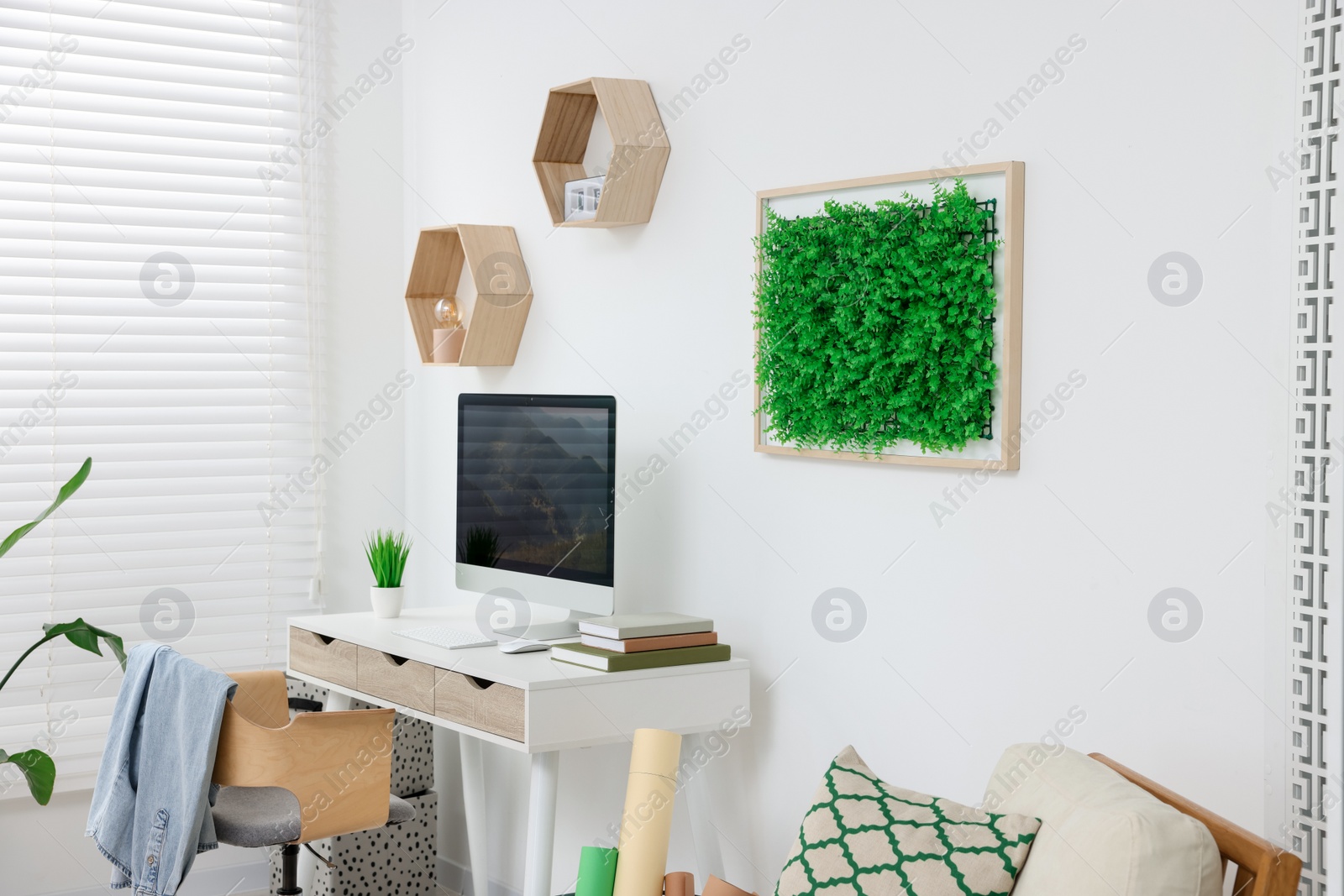 Photo of Green artificial plant wall panel and desk with computer in light room. Interior design