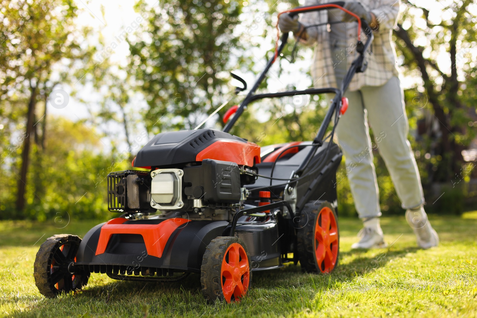 Photo of Woman cutting green grass with lawn mower in garden, selective focus