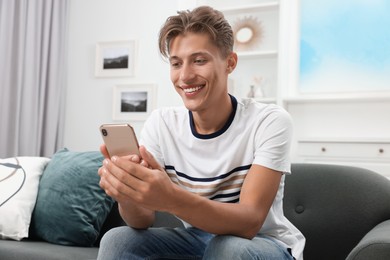 Photo of Happy young man having video chat via smartphone on sofa indoors