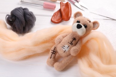 Photo of Felted bear, wool and tools on white wooden table, closeup