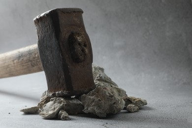 Photo of One sledgehammer and pieces of broken stones on grey background, closeup. Space for text