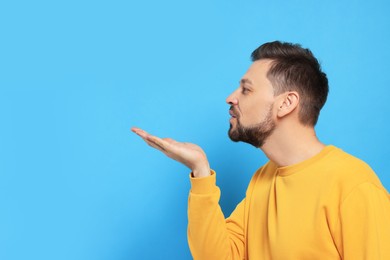 Photo of Handsome man blowing kiss on light blue background. Space for text