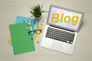 Blogger's workplace with laptop and stationery on white wooden background, flat lay