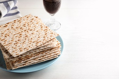 Photo of Stack of matzos and red wine on white table. Space for text