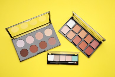 Photo of Different contouring palettes on yellow background, flat lay. Professional cosmetic product