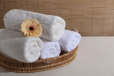 Photo of Rolled terry towels and flower on white table indoors, space for text