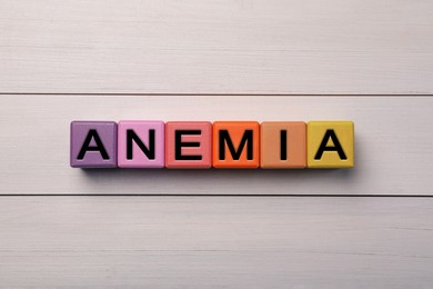 Photo of Word Anemia made with colorful cubes on white wooden table, flat lay