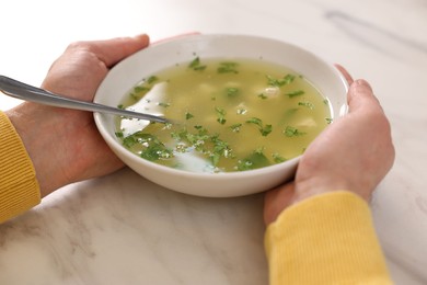 Man with bowl of delicious chicken soup at light marble table, closeup