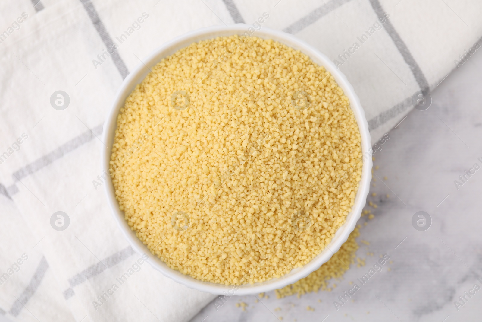 Photo of Raw couscous in bowl on light table, top view