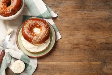 Photo of Delicious bagel with cream cheese on wooden table, flat lay. Space for text